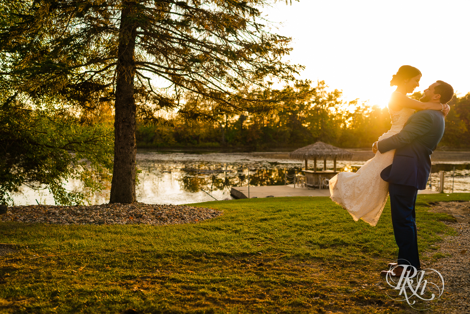 Groom lifts and kisses bride during sunset at The Chart House in Lakeville, Minnesota.