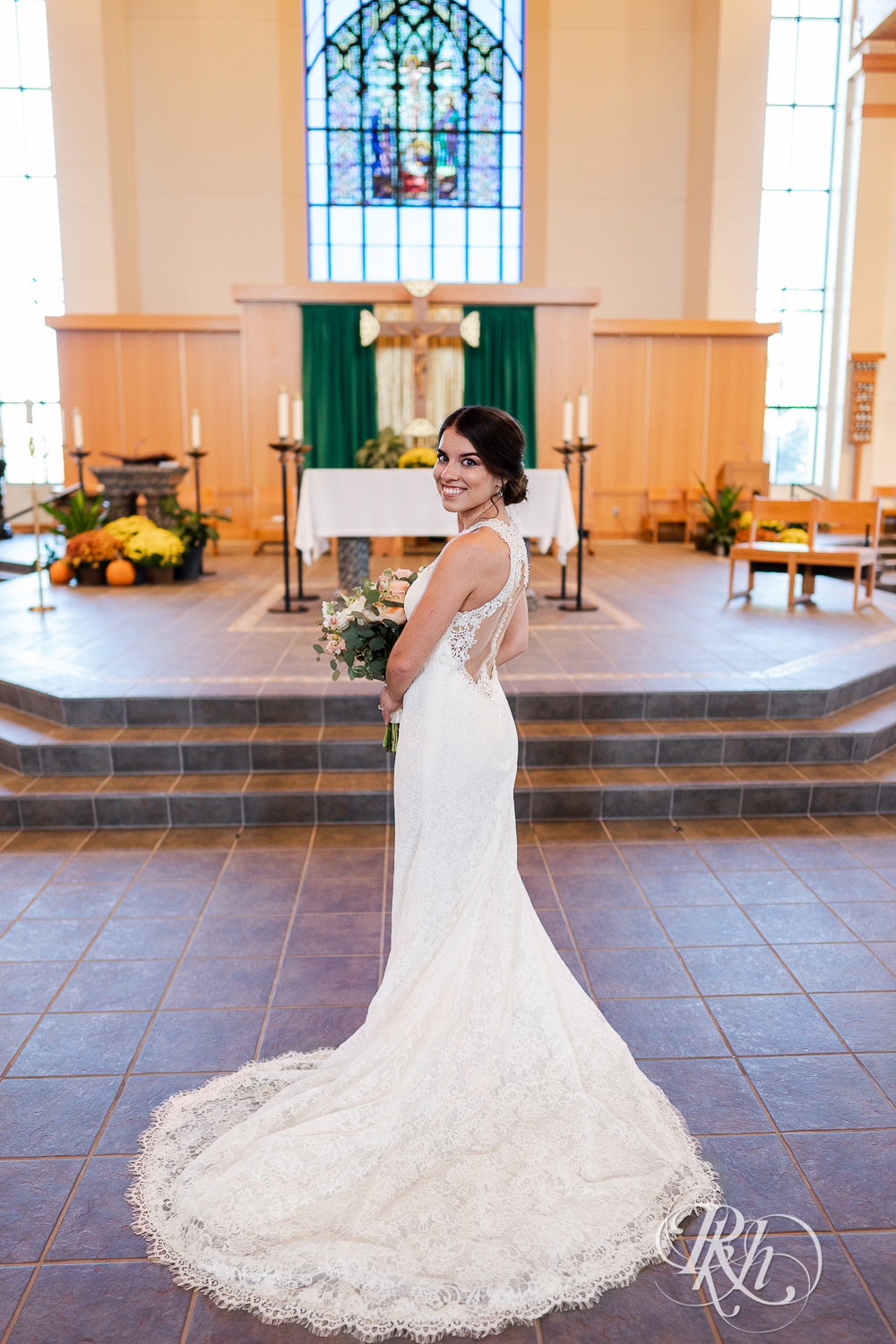 Bride holding flowers and looking over shoulder at Saint Joseph Catholic Church in Rosemount, Minnesota.