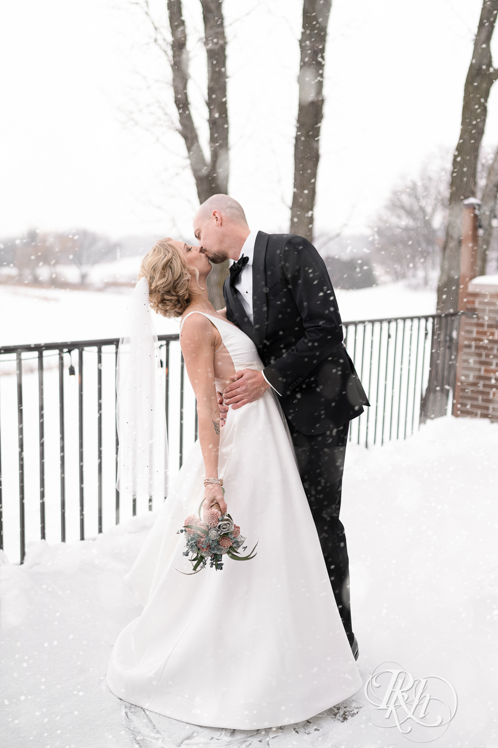 Bride and groom kissing in falling snow at Braemar Golf Course in Edina, Minnesota.