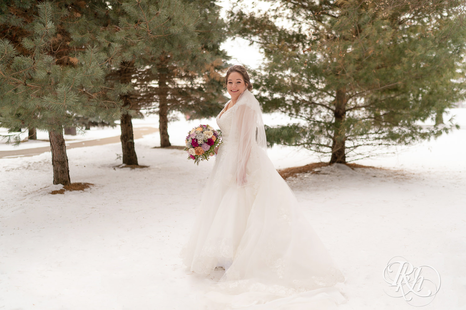Bride standing in snow, smiling and holding flowers at Glenhaven Events in Farmington, Minnesota.