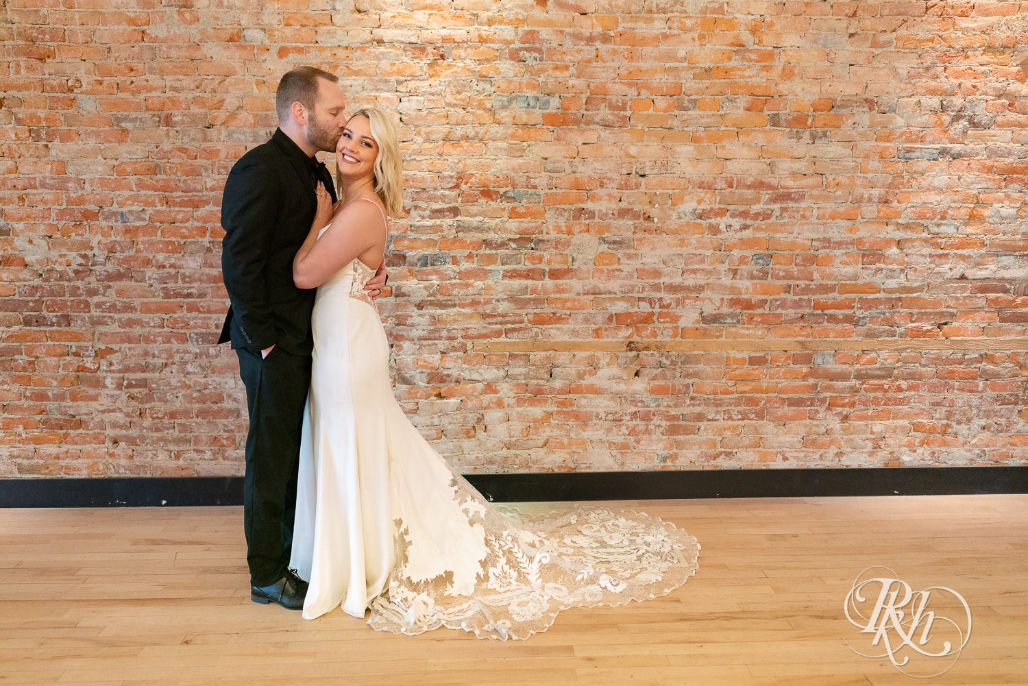 Bride and groom kissing in front of brick wall in 3 Ten Event Venue in Faribault, Minnesota.