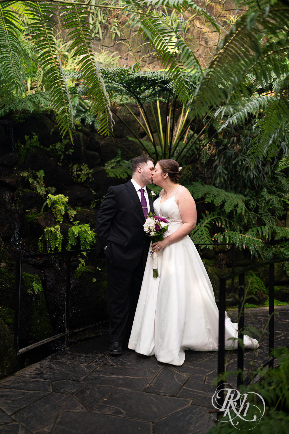 Bride and groom kissing among flowers at wedding at Como Zoo in Saint Paul, Minnesota.