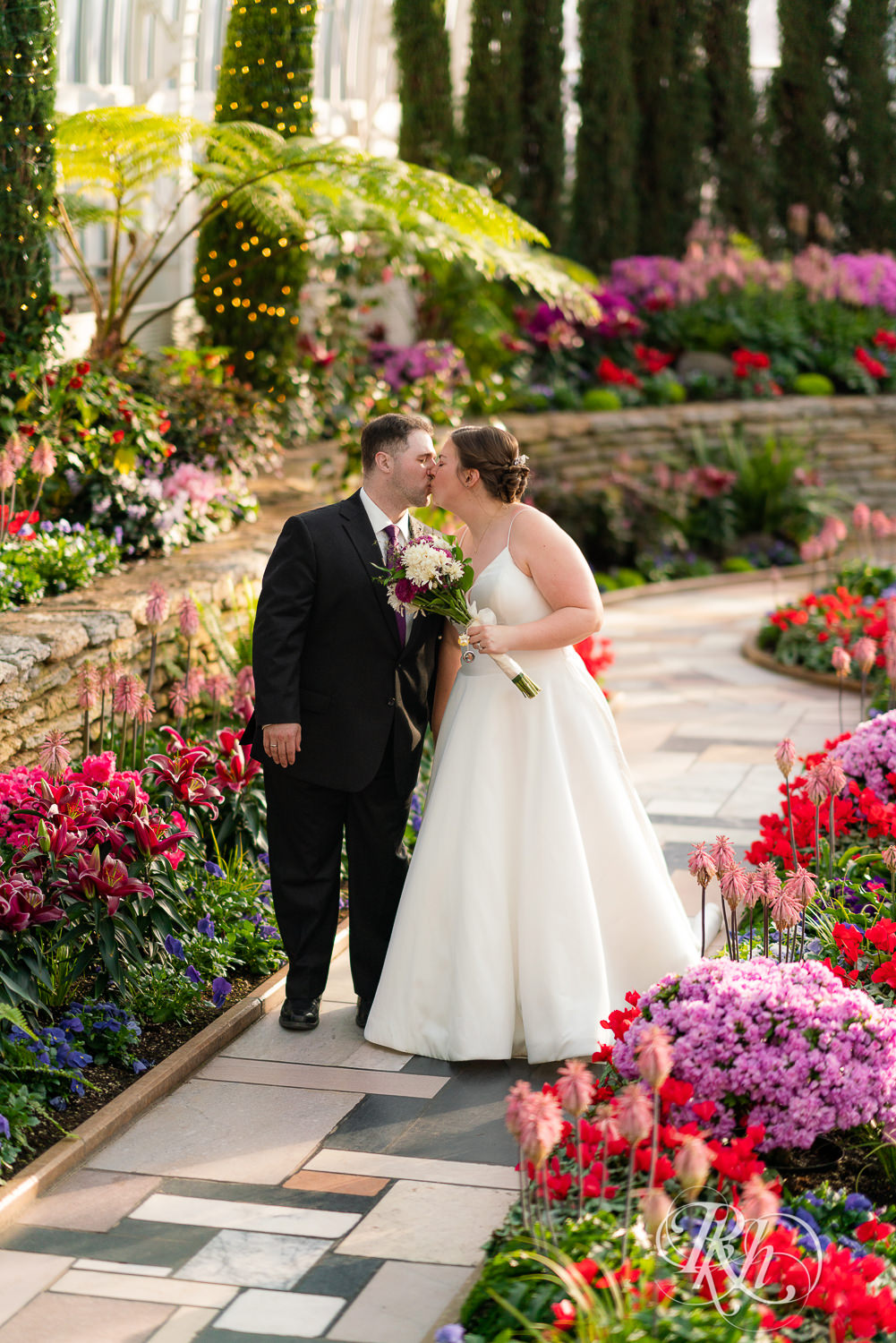 Bride and groom kissing among flowers at wedding at Como Zoo in Saint Paul, Minnesota.