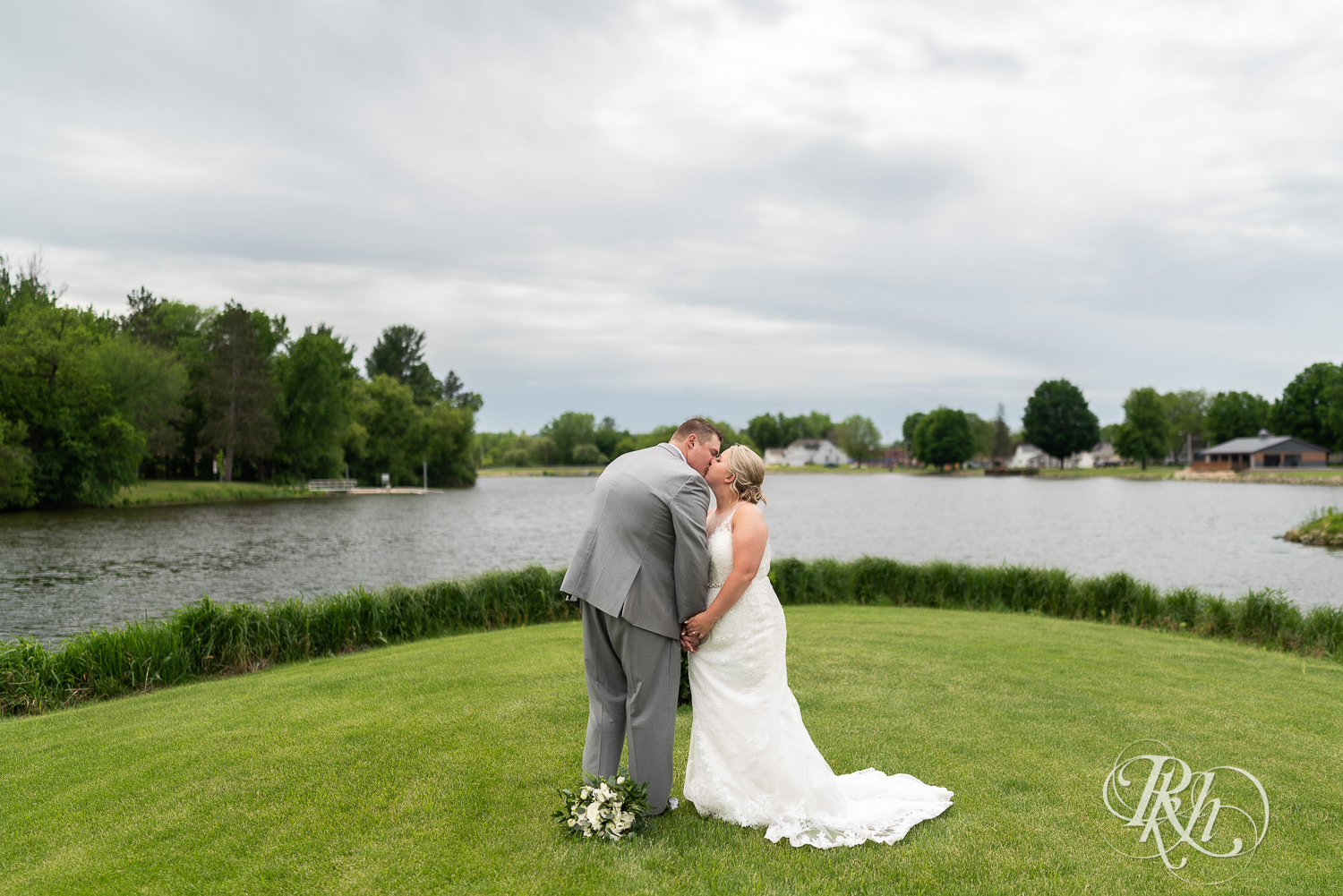 Bride and groom kiss in front of lake at Barn at Mirror Lake in Mondovi, Wisconsin.