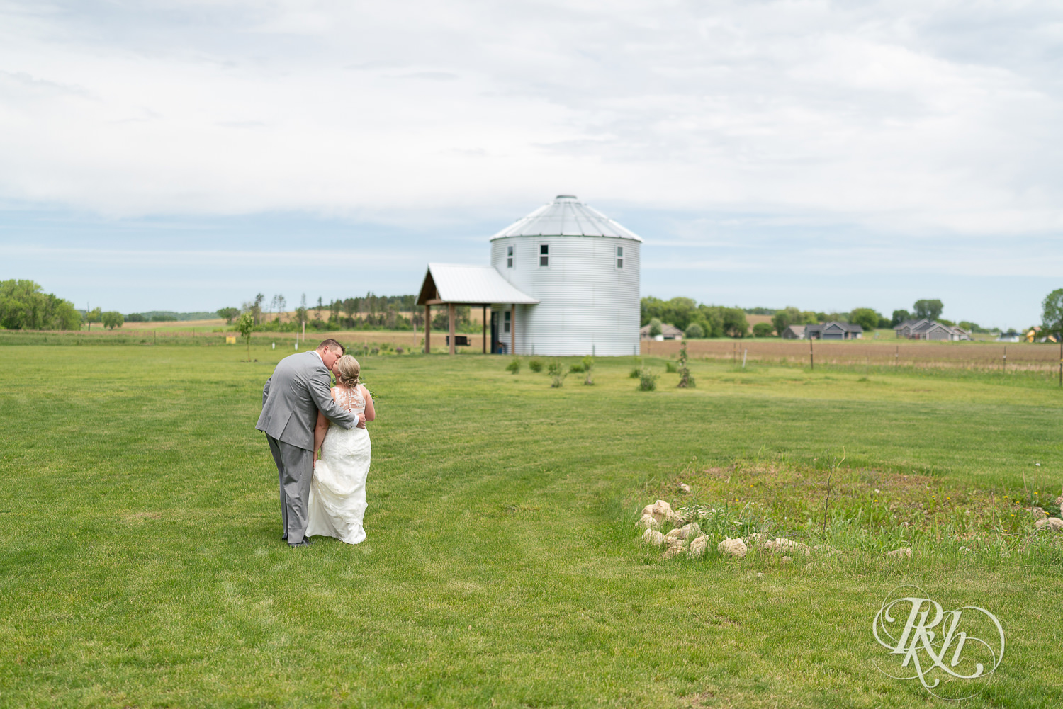 Bride and groom walk across field and kiss at Barn at Mirror Lake in Mondovi, Wisconsin.