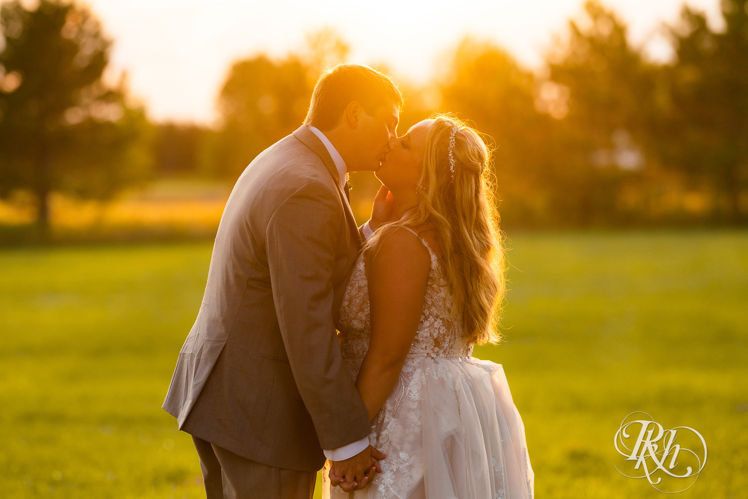Bride and groom kissing in a field at sunset