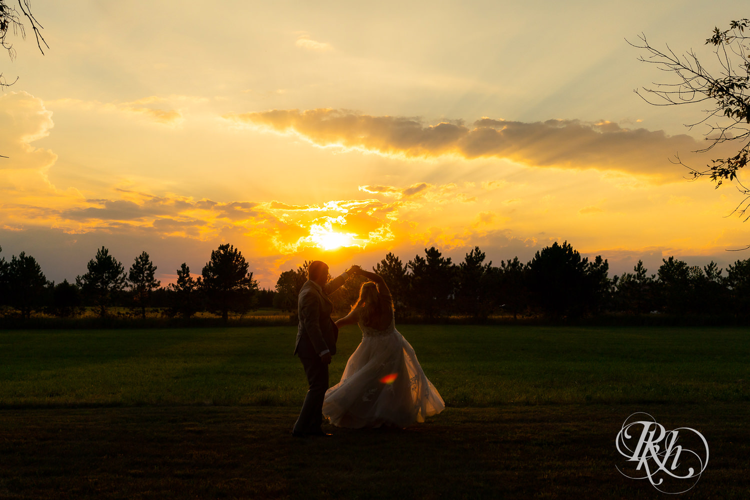 Bride and groom dancing in a field at sunset
