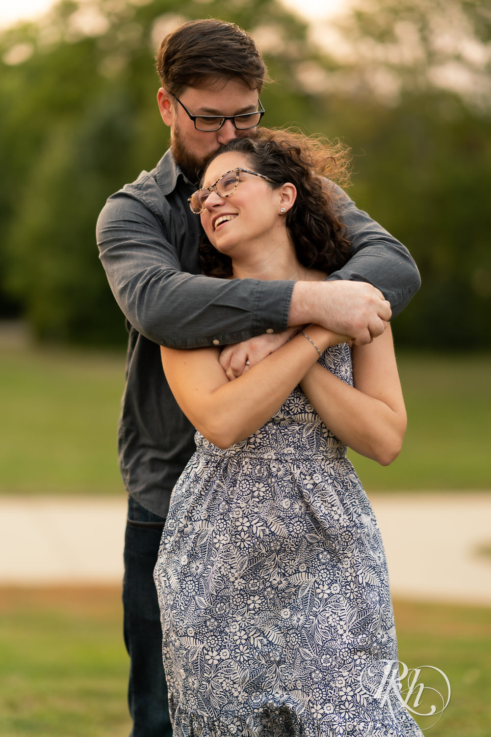 Man and woman in glasses holding each other at sunset engagement session.