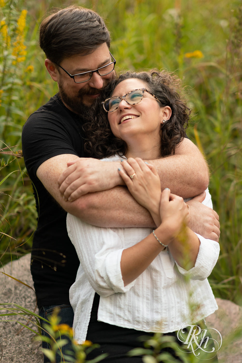 Man and woman in glasses holding each other at sunset engagement session.