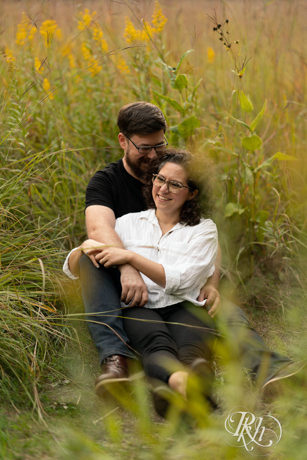 Man and woman in glasses holding each other in flower field.