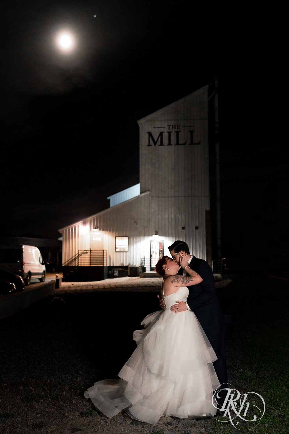 Bride and groom kissing in front of The Mill Events in Chetek, Wisconsin at night with a full moon.