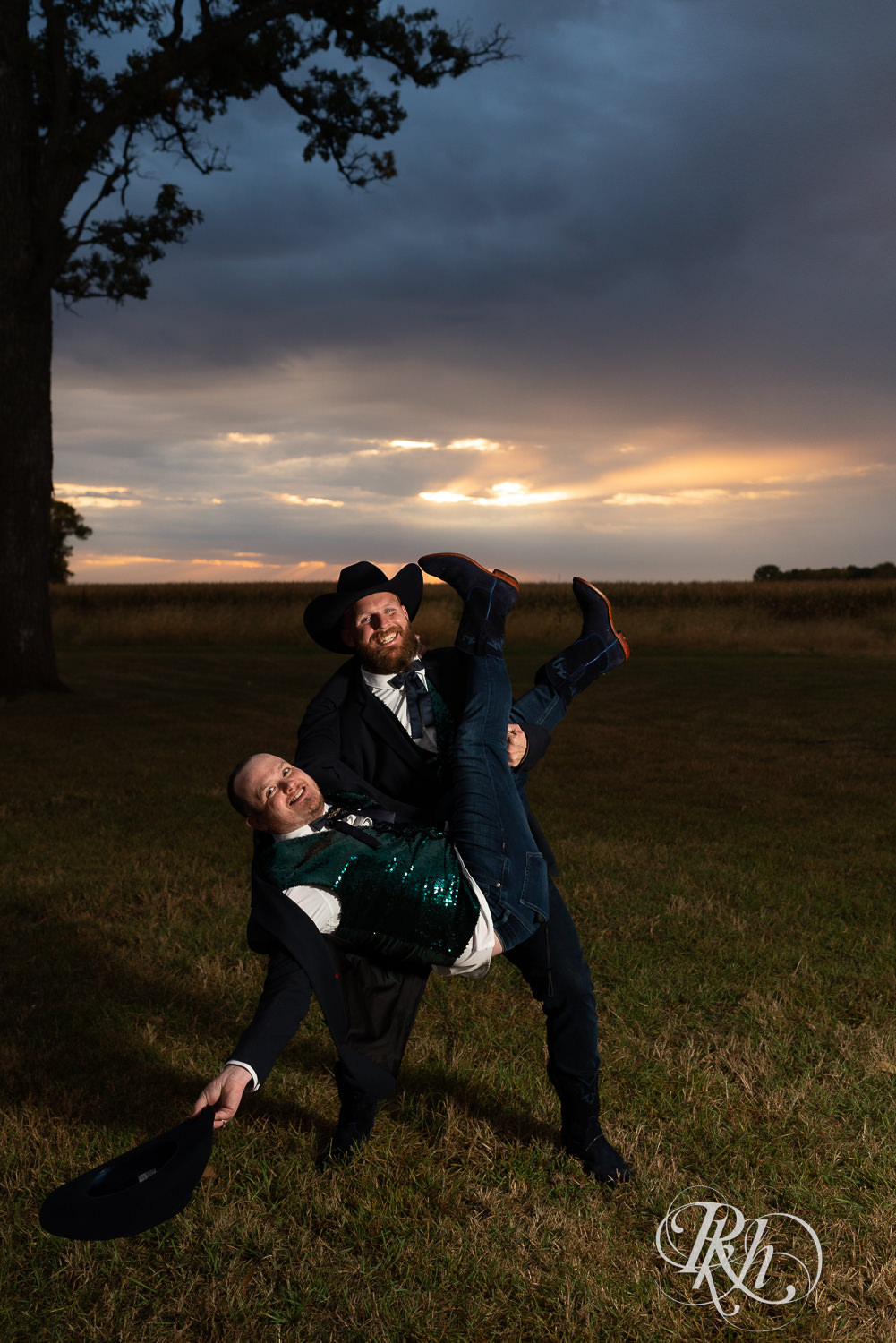 Groom carrying other groom during sunset on their wedding day.