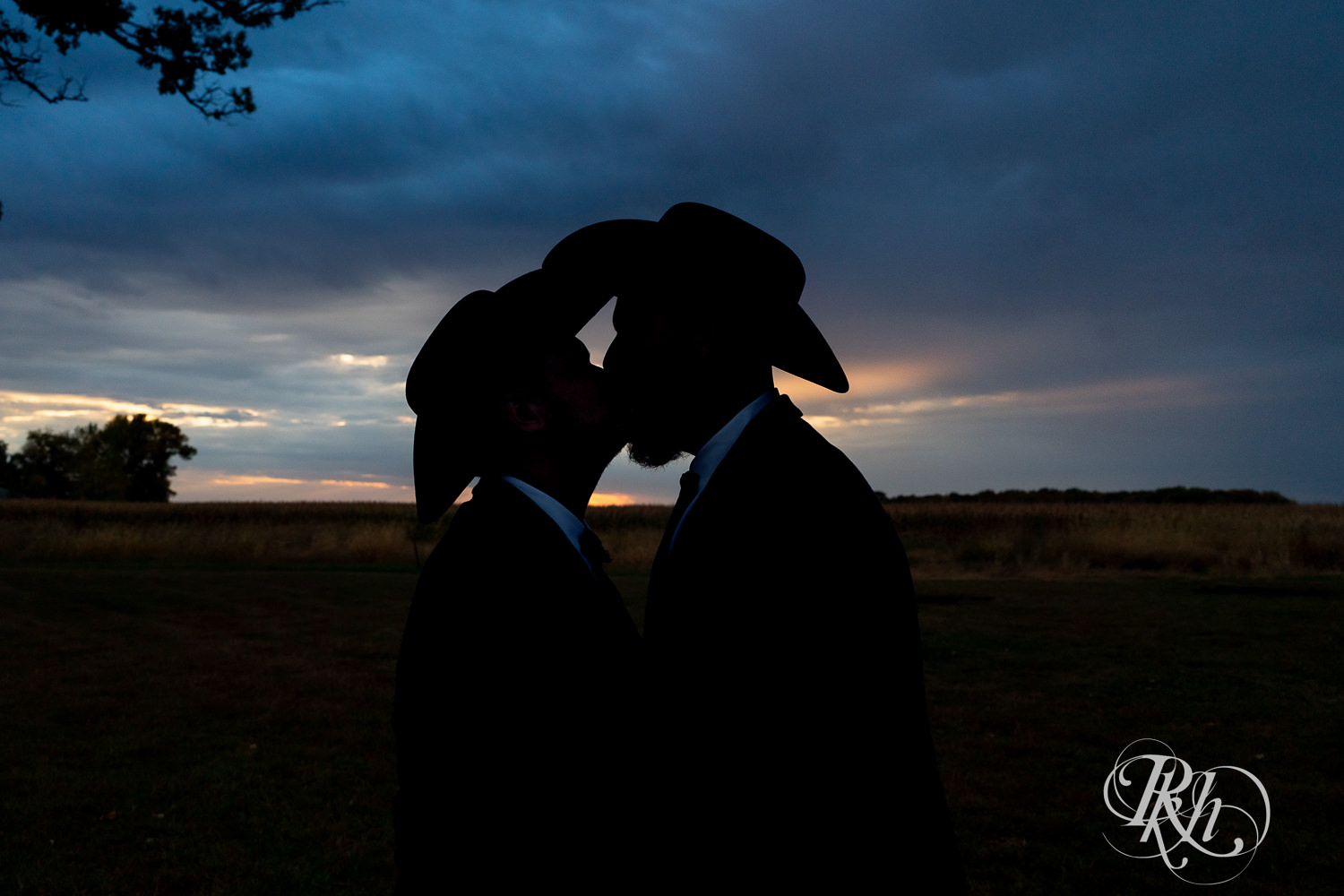 Grooms in cowboy hats kissing in silhouette on their wedding day.
