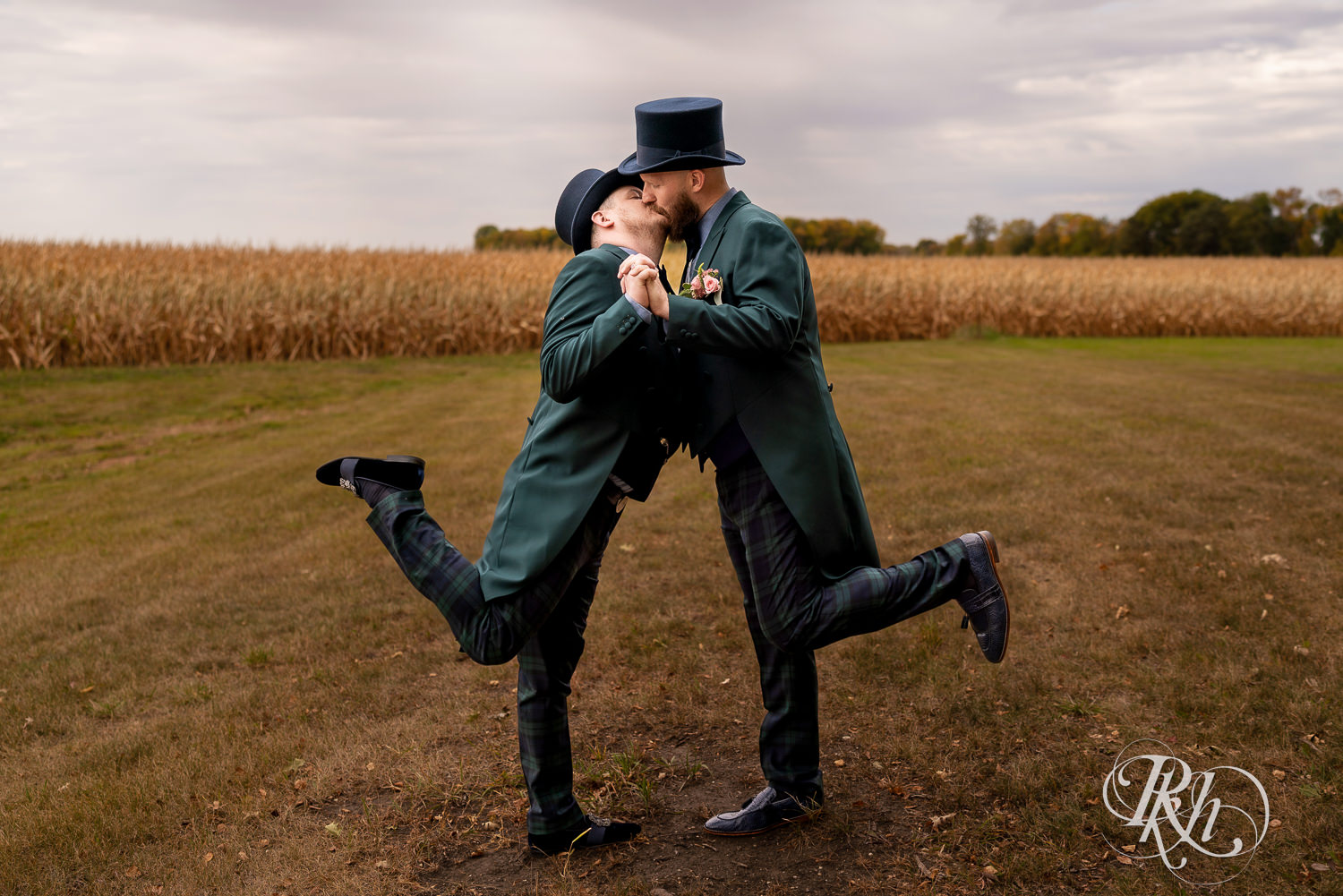 Grooms kissing and holding hands in field on their wedding day.