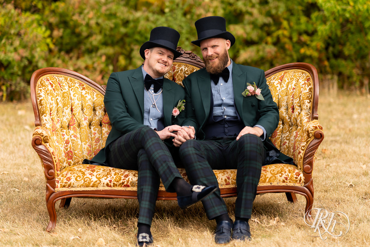 Grooms sitting on couch in field smiling and looking at the camera.