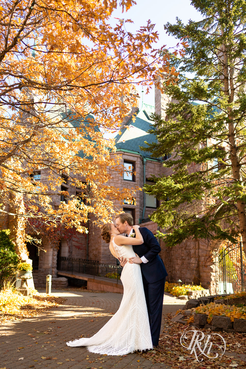 Redheaded bride and groom dip and kiss in front of the Van Dusen Mansion in Minneapolis, Minnesota in the fall.