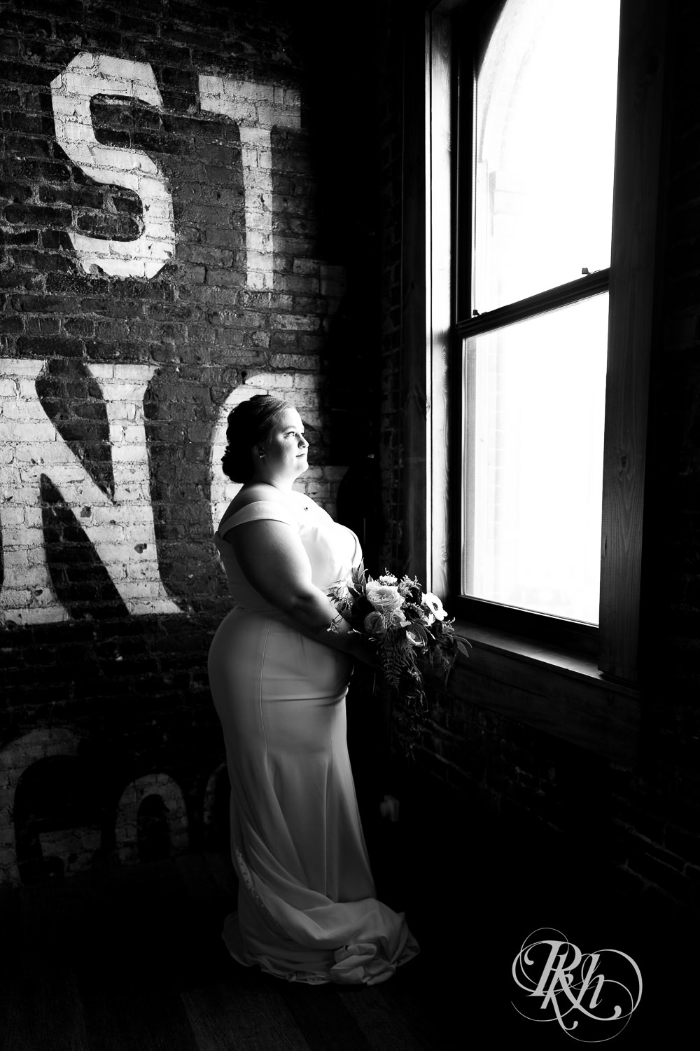 Bride holding bouquet while looking out the window of Earl and Wilson Event Center in Saint Paul, Minnesota.