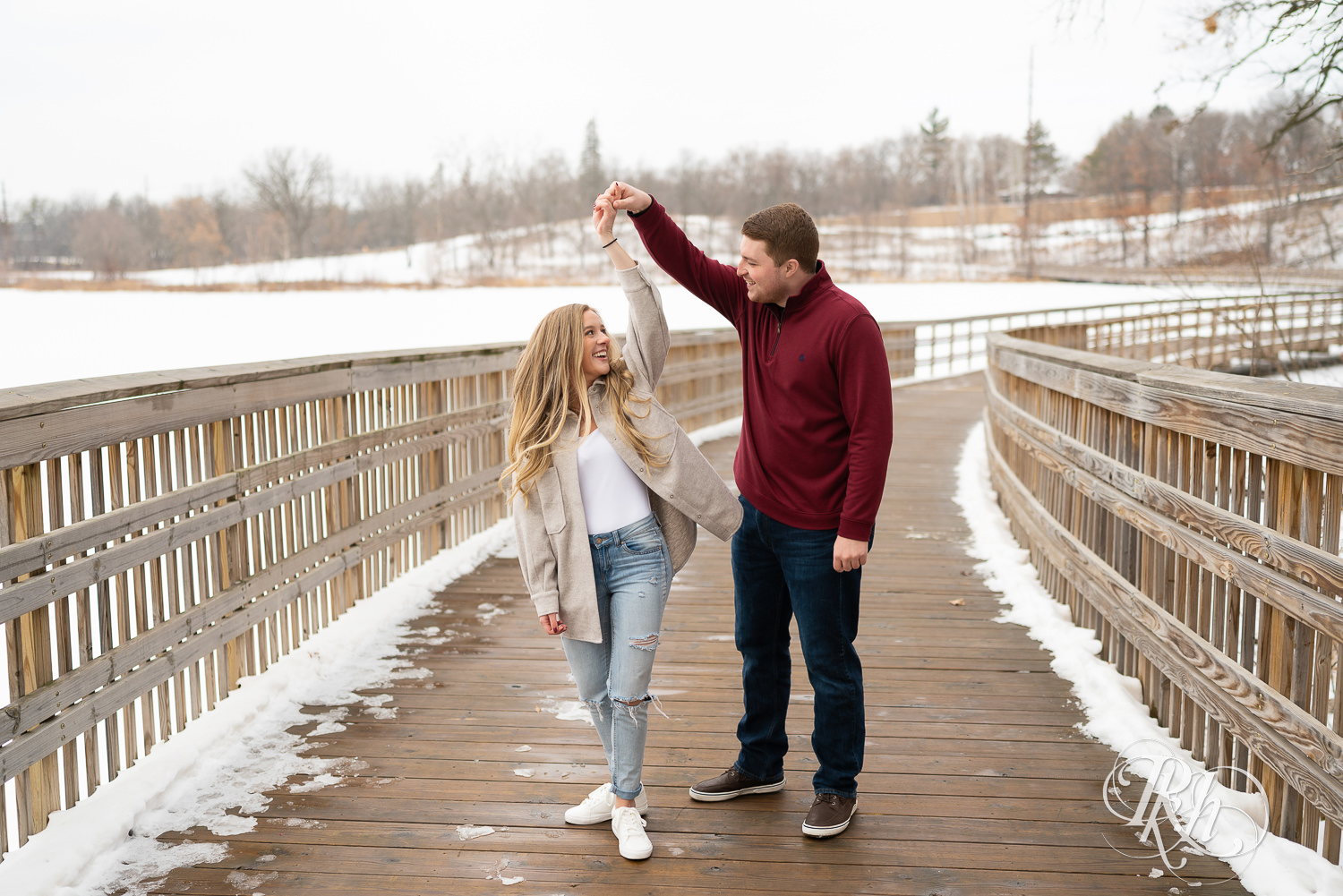 Man spins woman on a bridge in winter engagement photo.