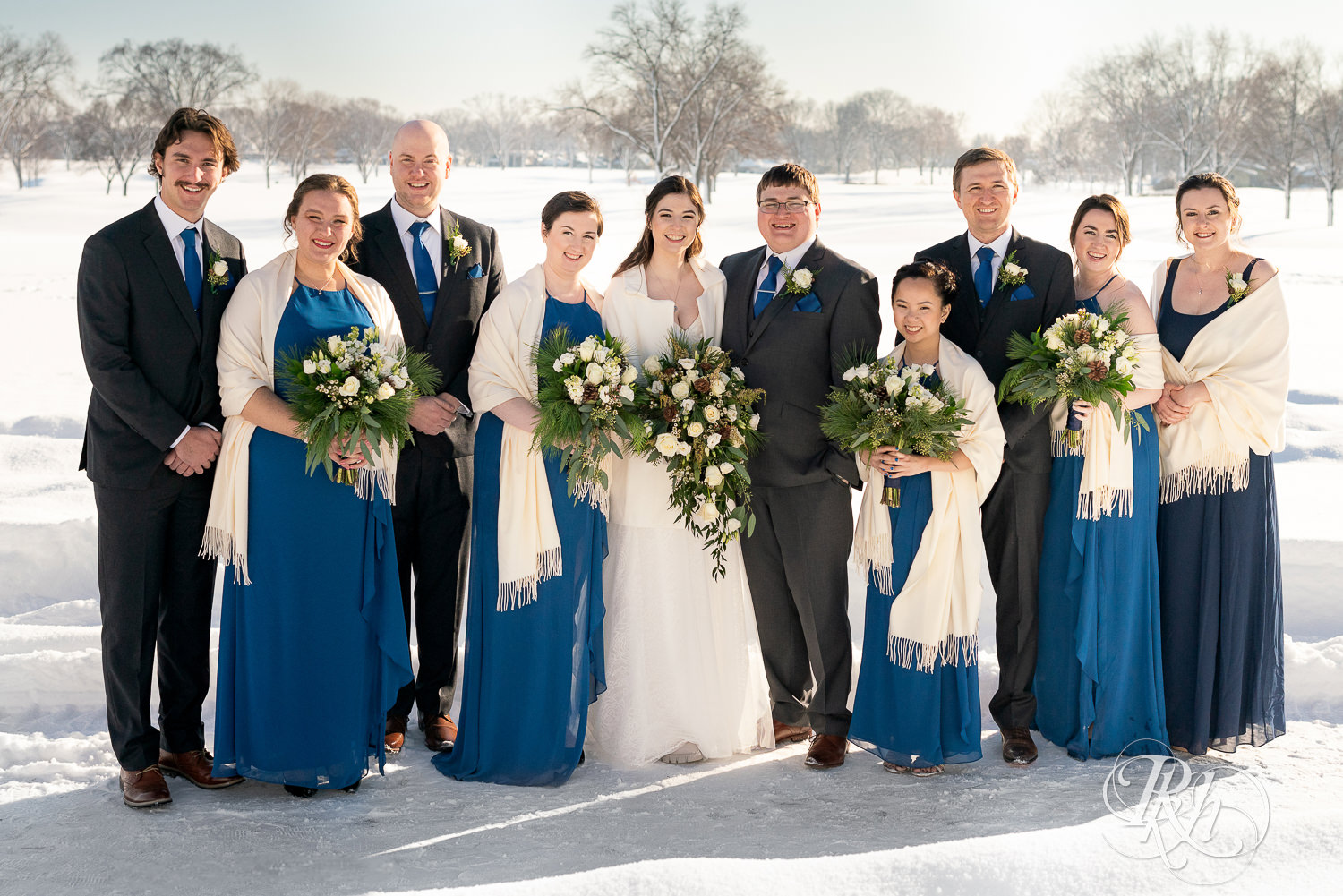 Wedding party in blue dresses and grey suits in the snow at Minneapolis Golf Club in Saint Louis Park, Minnesota.