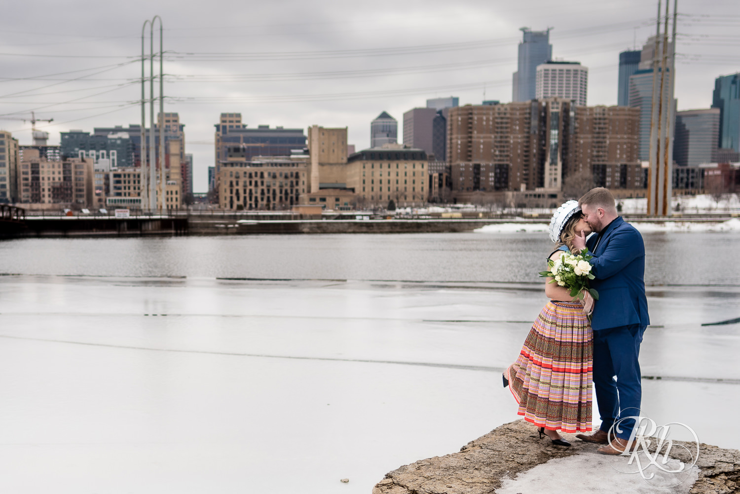 Man and Hmong woman kiss in Saint Anthony Main in Minneapolis, Minnesota with city in the background.
