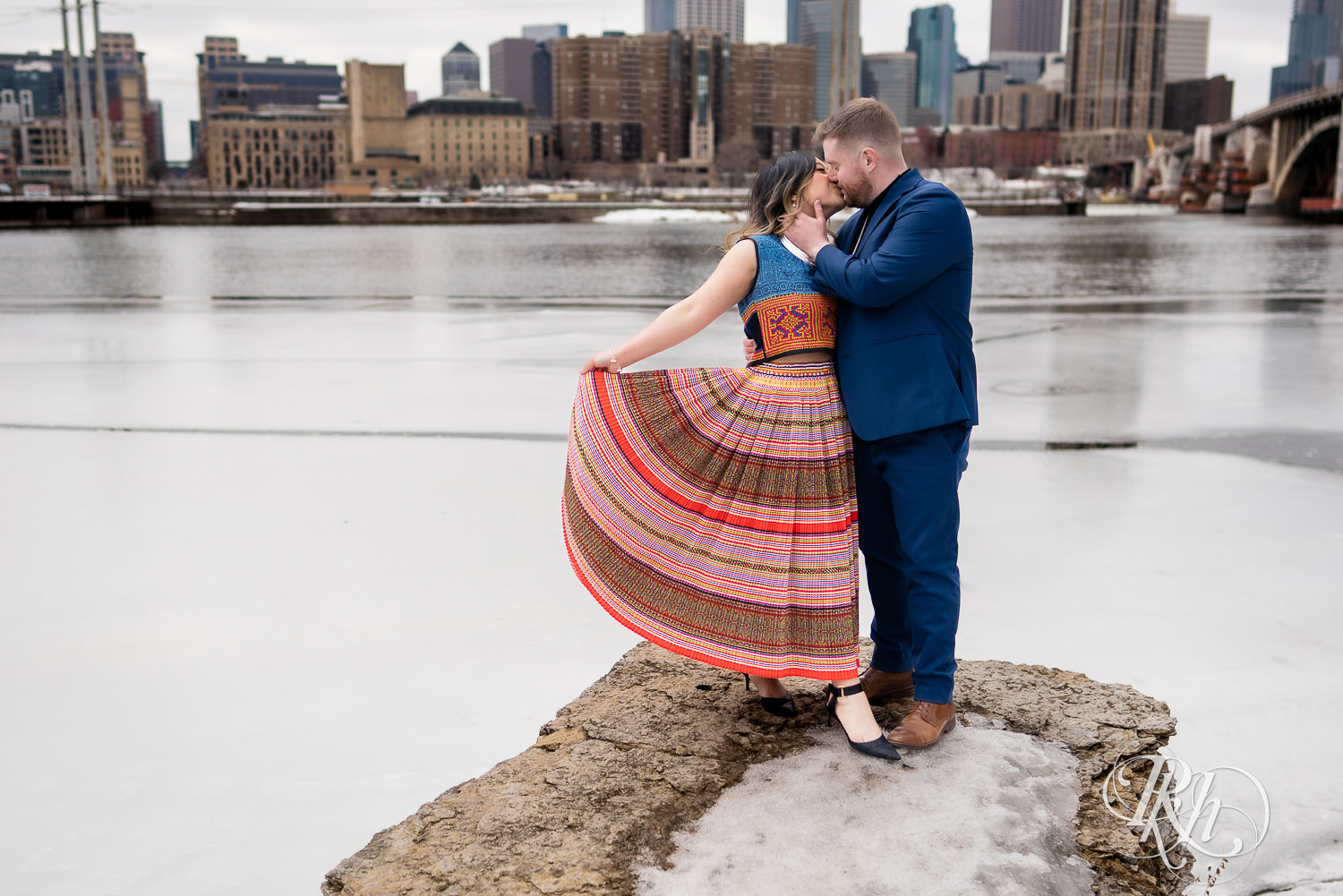 Man and Hmong woman kiss in Saint Anthony Main in Minneapolis, Minnesota with city in the background.
