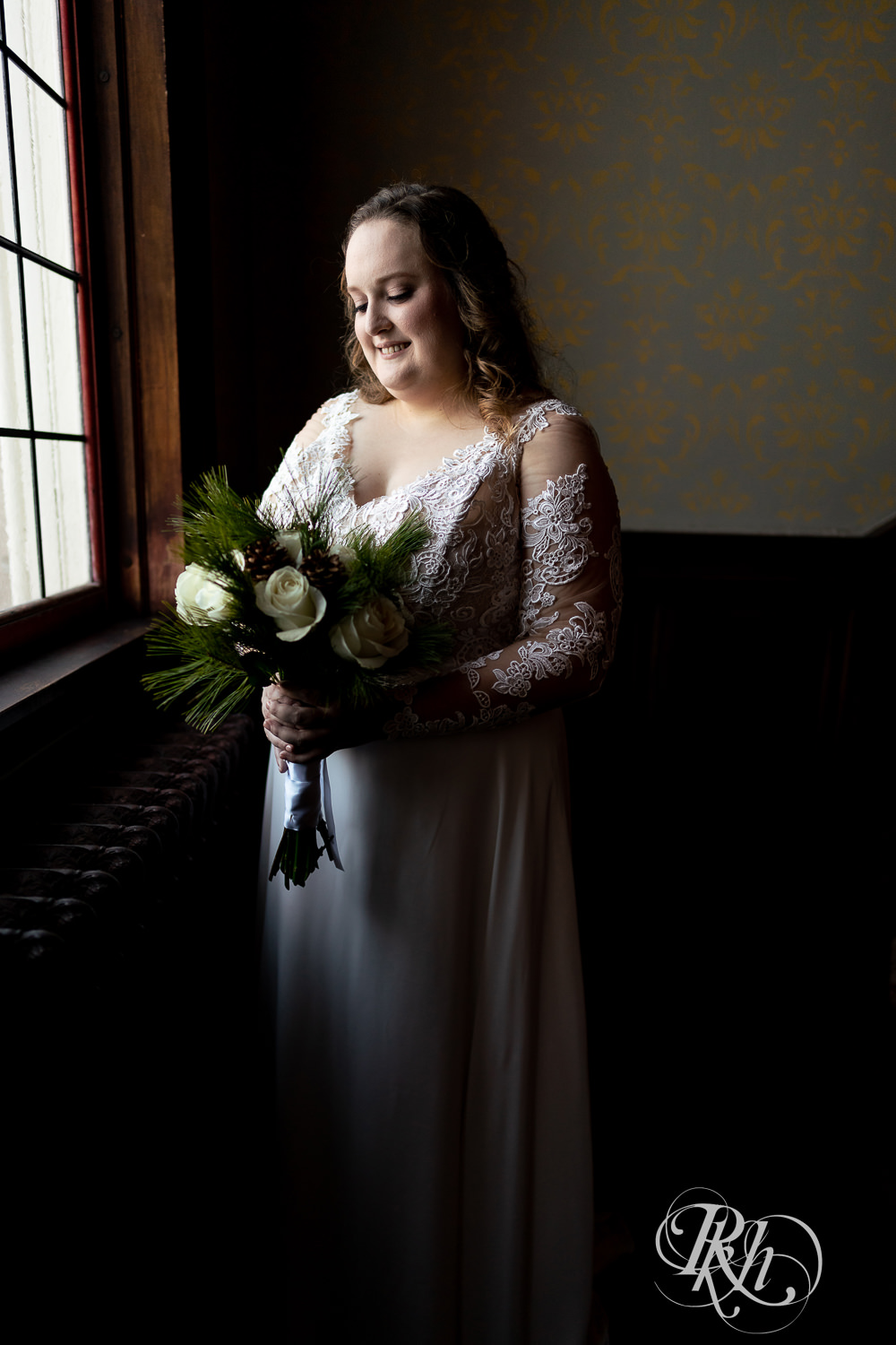 Bride holding flowers standing next to window at Semple Mansion in Minneapolis, Minnesota.