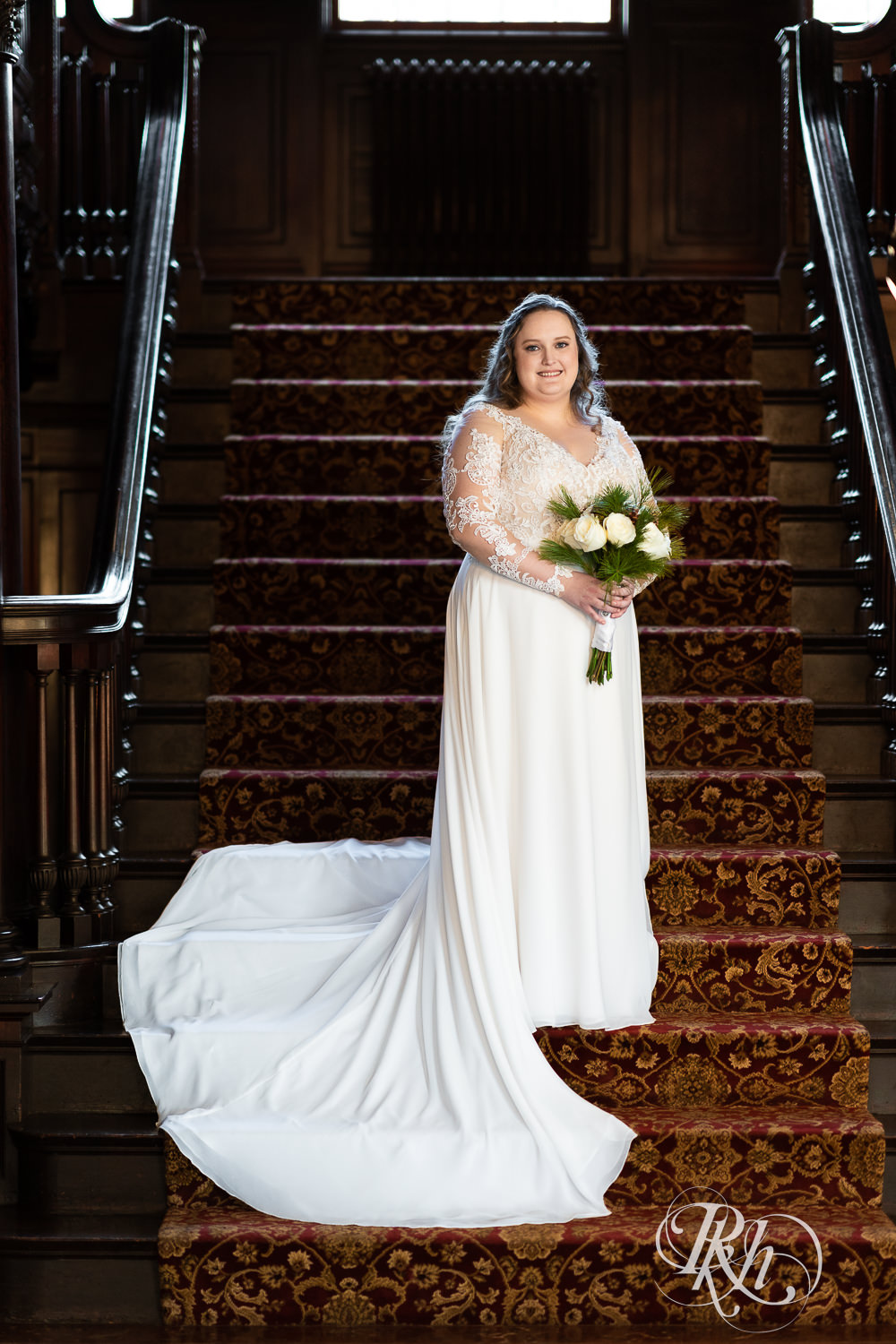Bride holding flowers standing on grand staircase at Semple Mansion in Minneapolis, Minnesota.