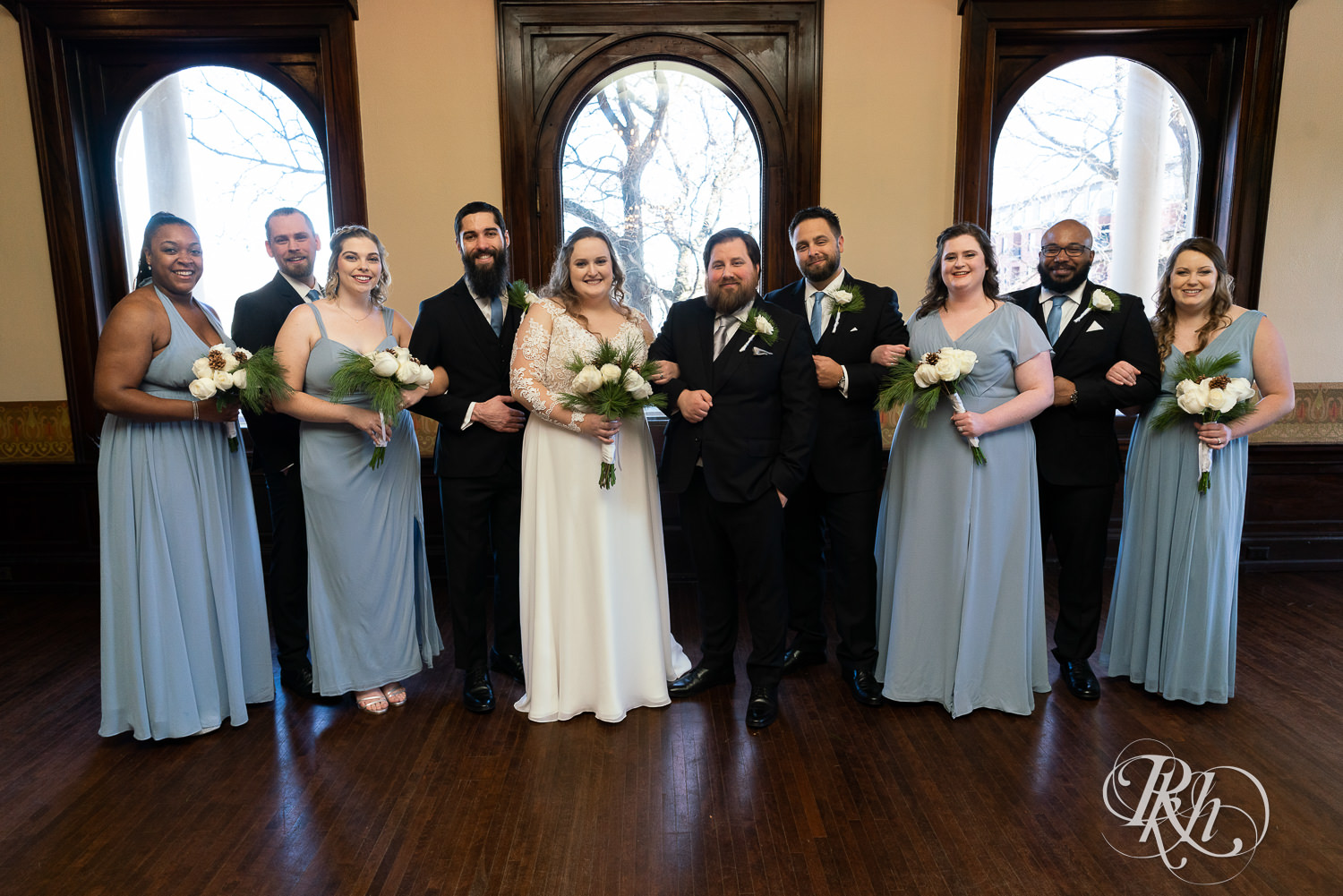 Wedding party in black suits and blue dresses smiling at Semple Mansion in Minneapolis, Minnesota.