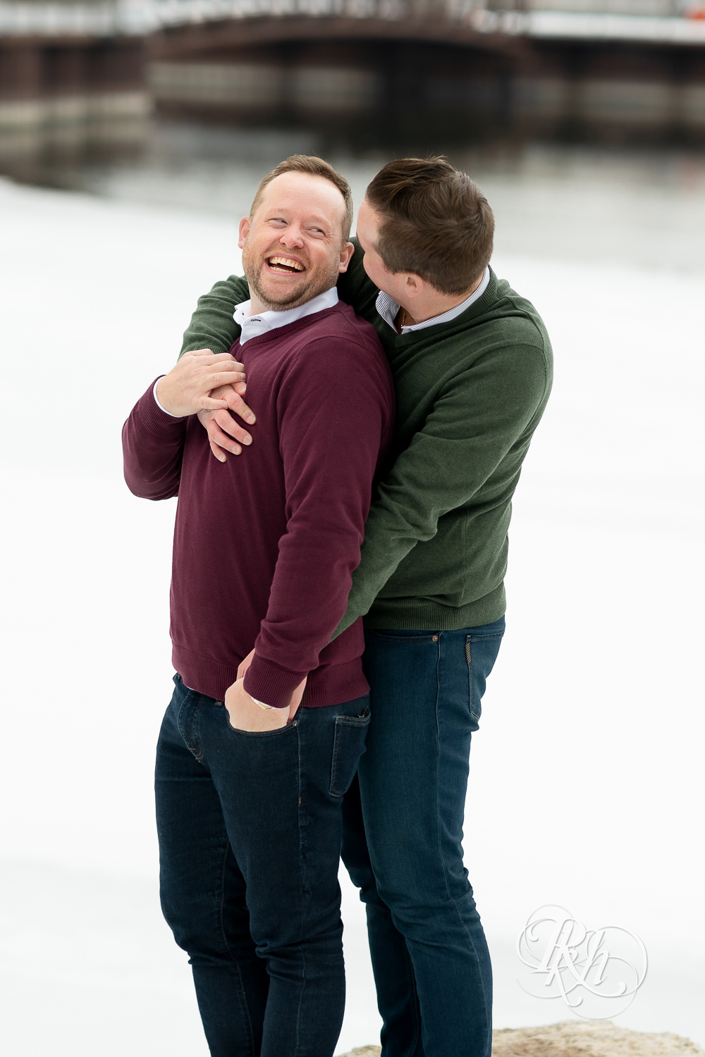 Gay men smile in snow during the winter in Minneapolis, Minnesota with city in background.