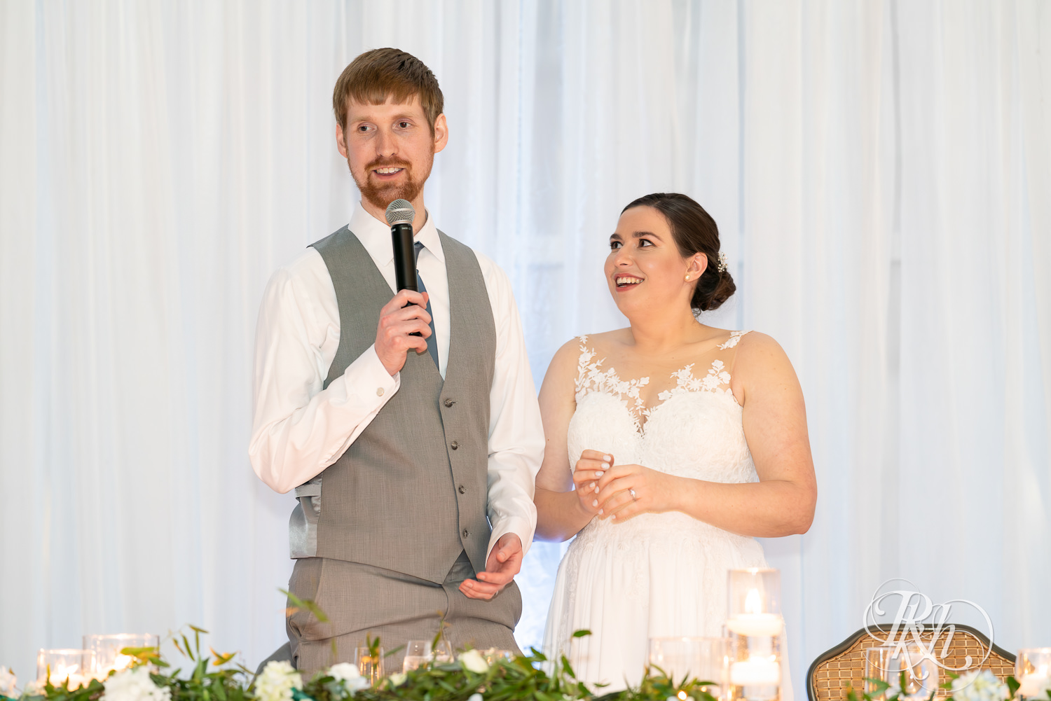 Bride and groom smile during wedding speeches at Doubletree Hilton Saint Paul in Saint Paul, Minnesota.