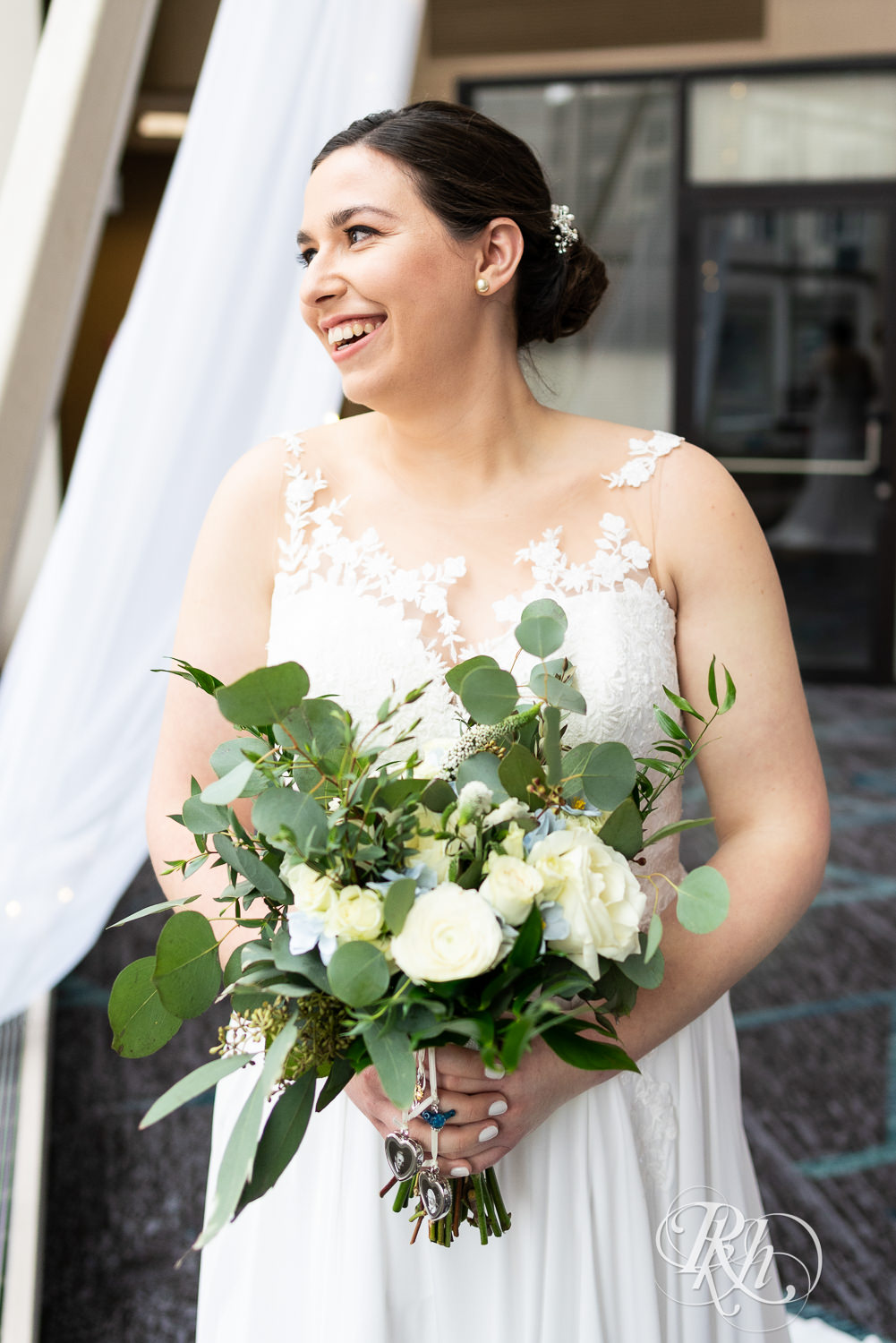 Bride holding flowers and smiling out window at Doubletree Hilton Saint Paul in Saint Paul, Minnesota.