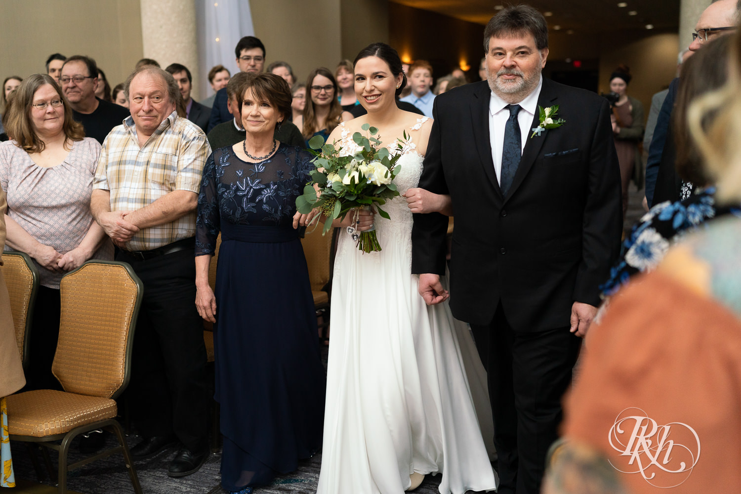 Bride walks down the aisle with parents at Doubletree Hilton Saint Paul in Saint Paul, Minnesota.
