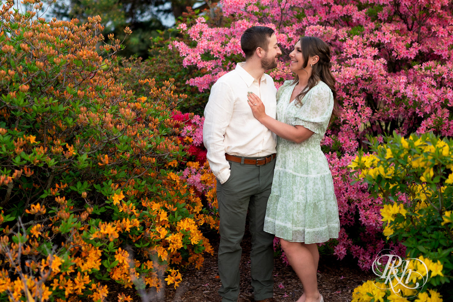 Man in white shirt and woman in green dress smile in front of flowers at the Minnesota Landscape Arboretum in Chaska, Minnesota.