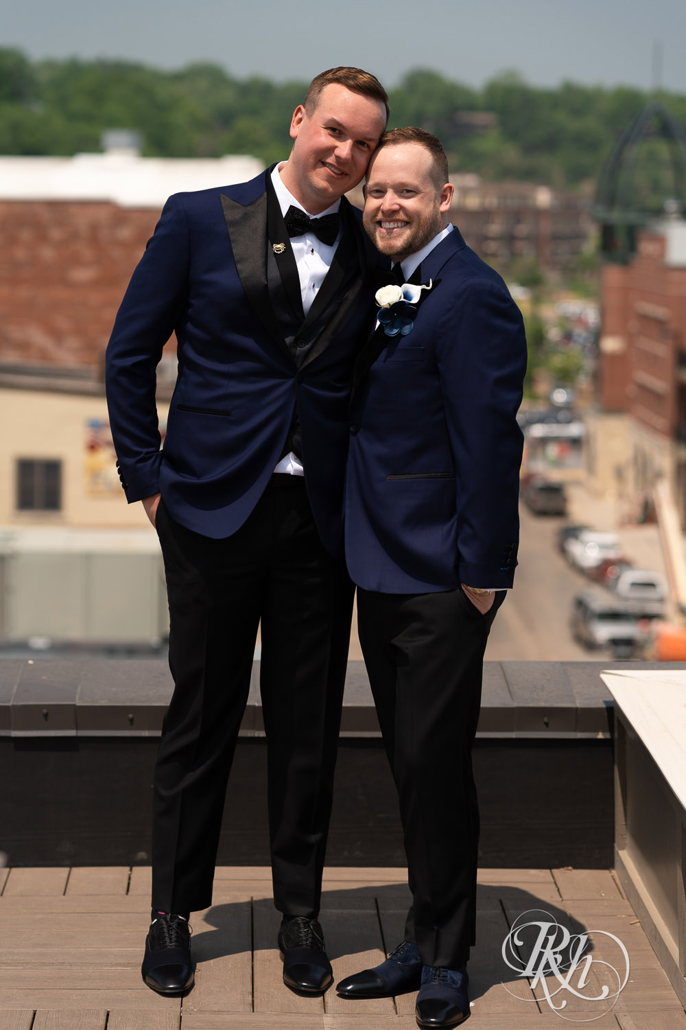 Grooms in blue suits smile on rooftop before gay wedding in Stillwater, Minnesota.