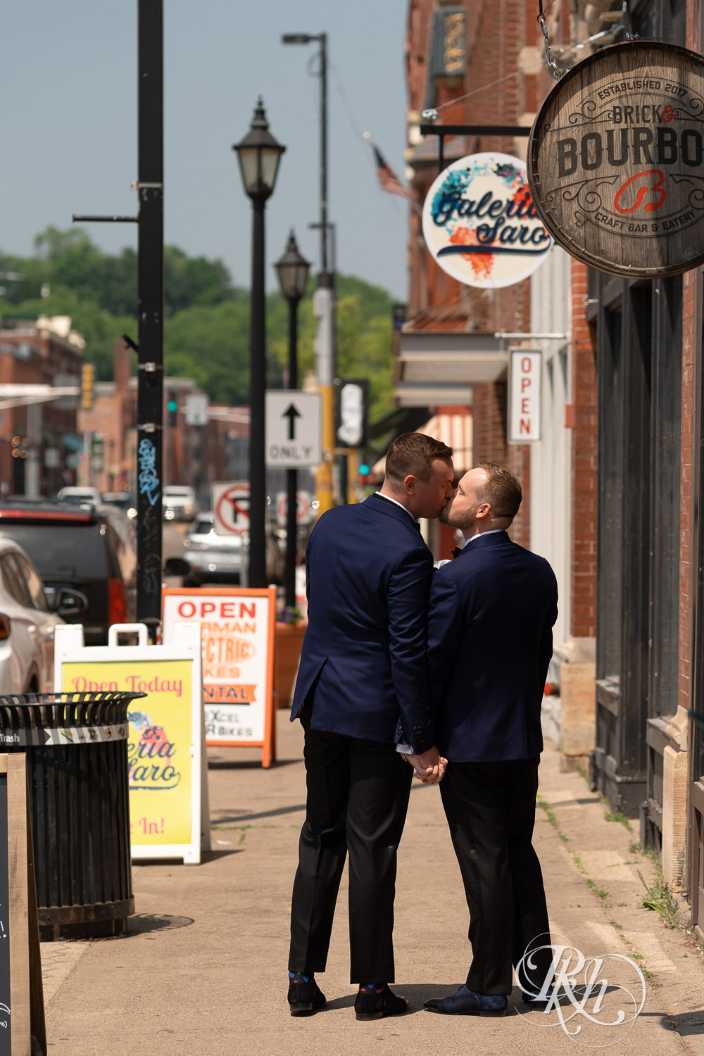 Grooms in blue suits kiss walking down the street before gay wedding in Stillwater, Minnesota.