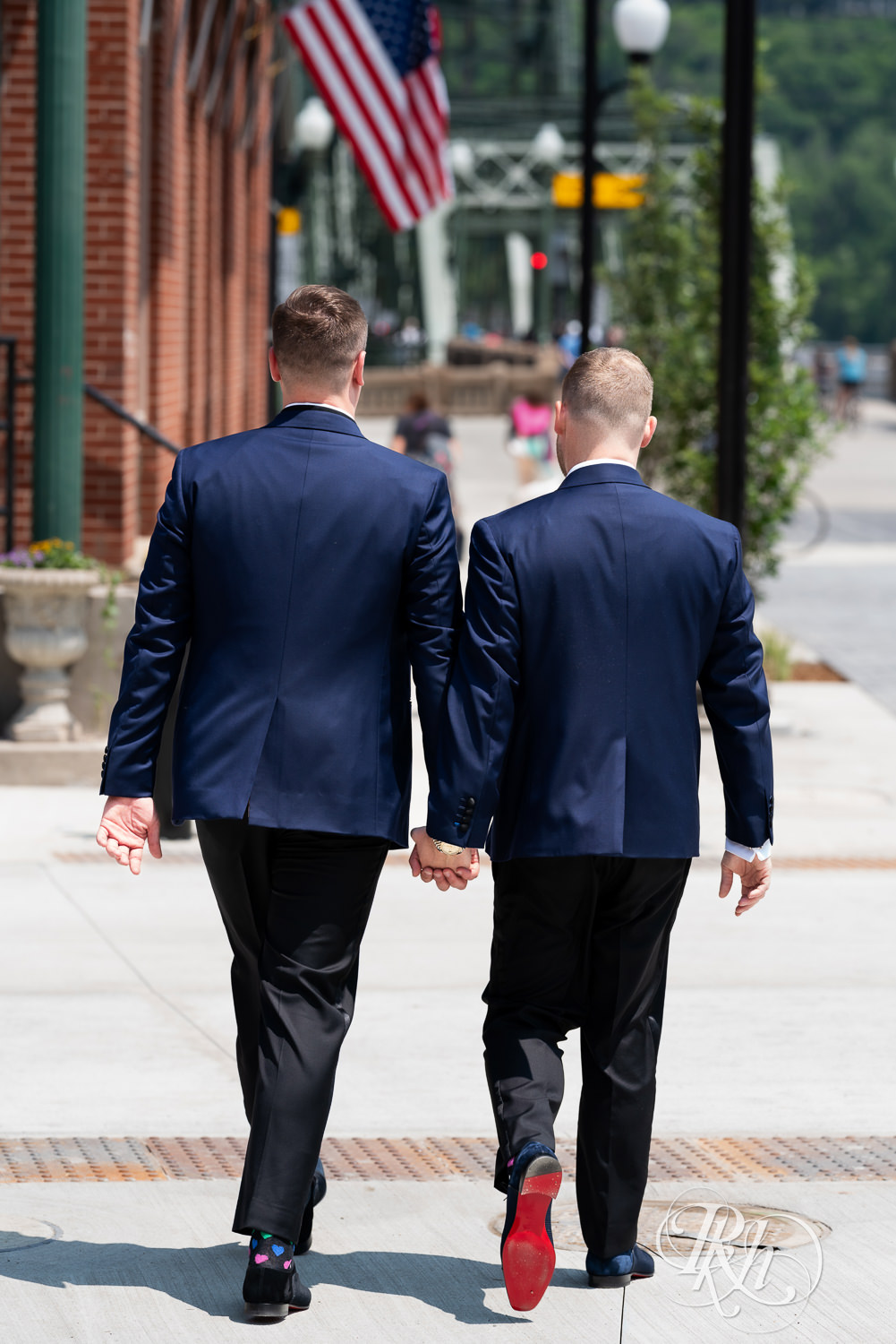 Grooms in blue suits hold hands walking down the street before gay wedding in Stillwater, Minnesota.