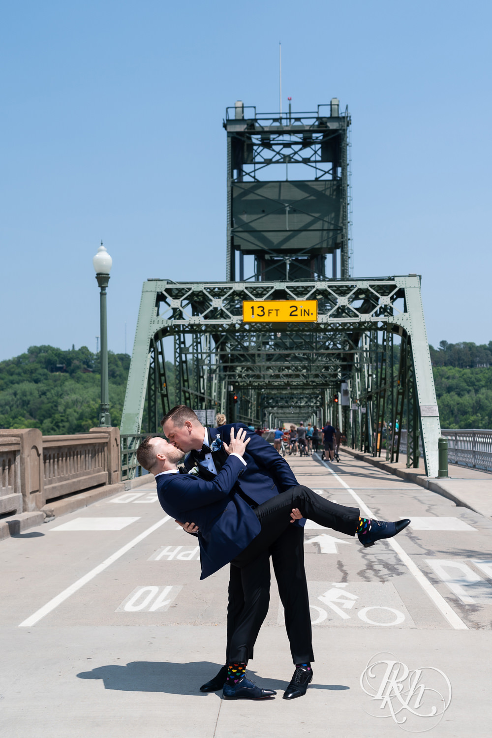 Grooms in blue tuxedos kiss on bridge before gay wedding in Stillwater, Minnesota.