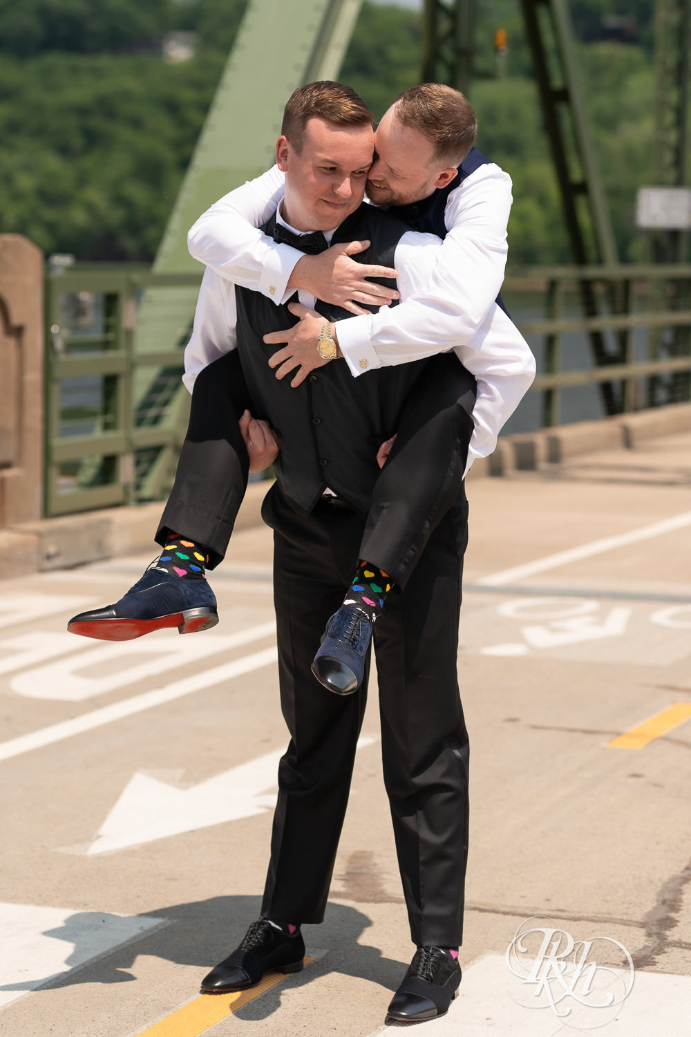 Grooms in blue tuxedos hold hands on bridge before gay wedding in Stillwater, Minnesota.