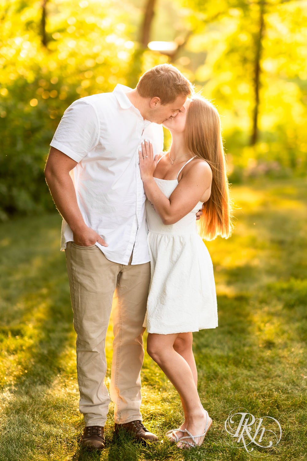Man in white shirt and woman in white dress kiss during golden hour engagement photography at Lebanon Hills in Eagan, Minnesota.