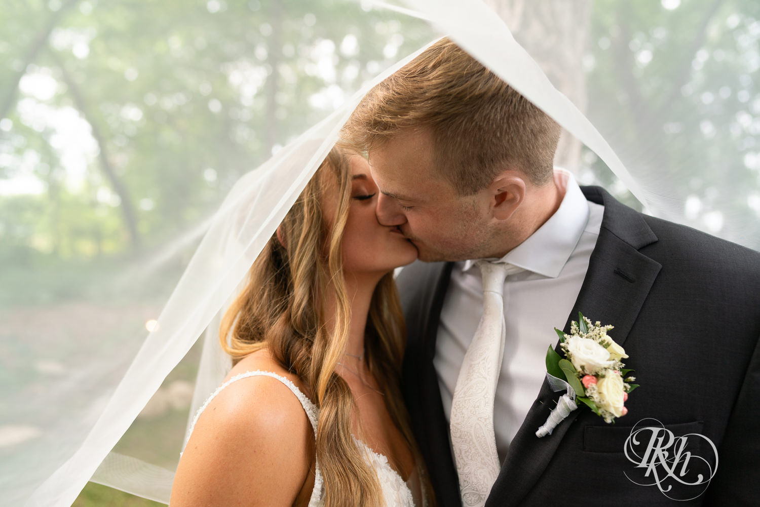 Bride and groom kiss under veil on wedding day at Ahavah Cottage in Elysian, Minnesota.
