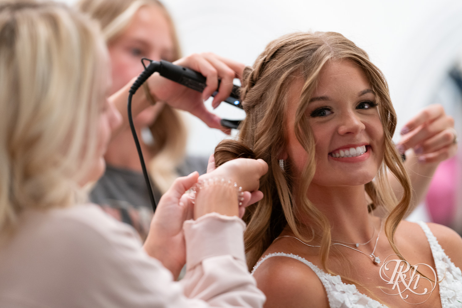 Bride smiling while getting hair curled on wedding day at Ahavah Cottage in Elysian, Minnesota.