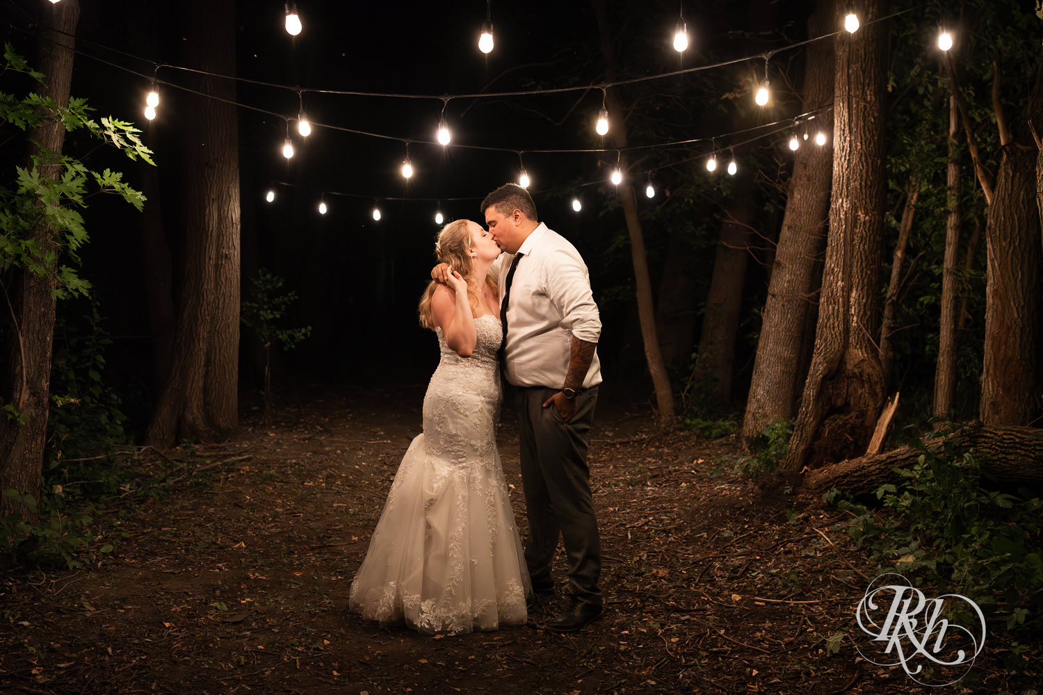 Bride and groom kiss under lights at night at Cottage Farmhouse in Glencoe, Minnesota.
