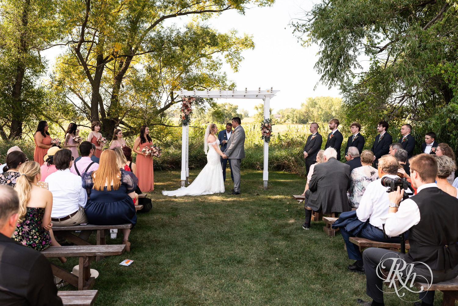 Bride and groom hold hands during summer wedding ceremony at Cottage Farmhouse in Glencoe, Minnesota.