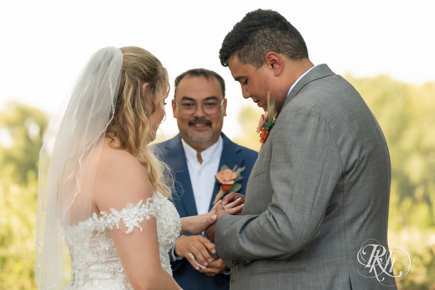 Bride and groom exchange rings during summer wedding ceremony at Cottage Farmhouse in Glencoe, Minnesota.