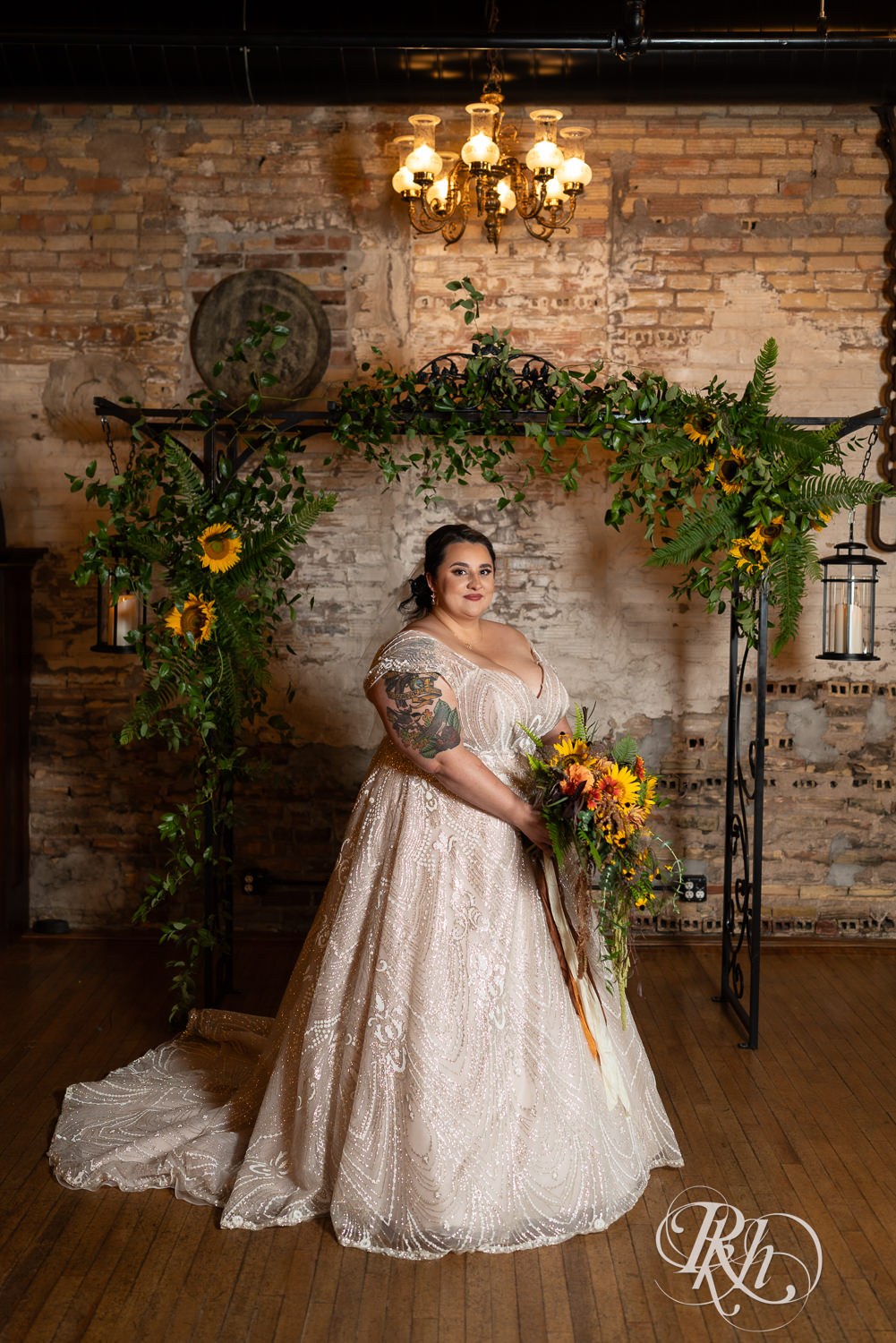 Plus size bride smiles in front of flower arch at Kellerman's Event Center in White Bear Lake, Minnesota.
