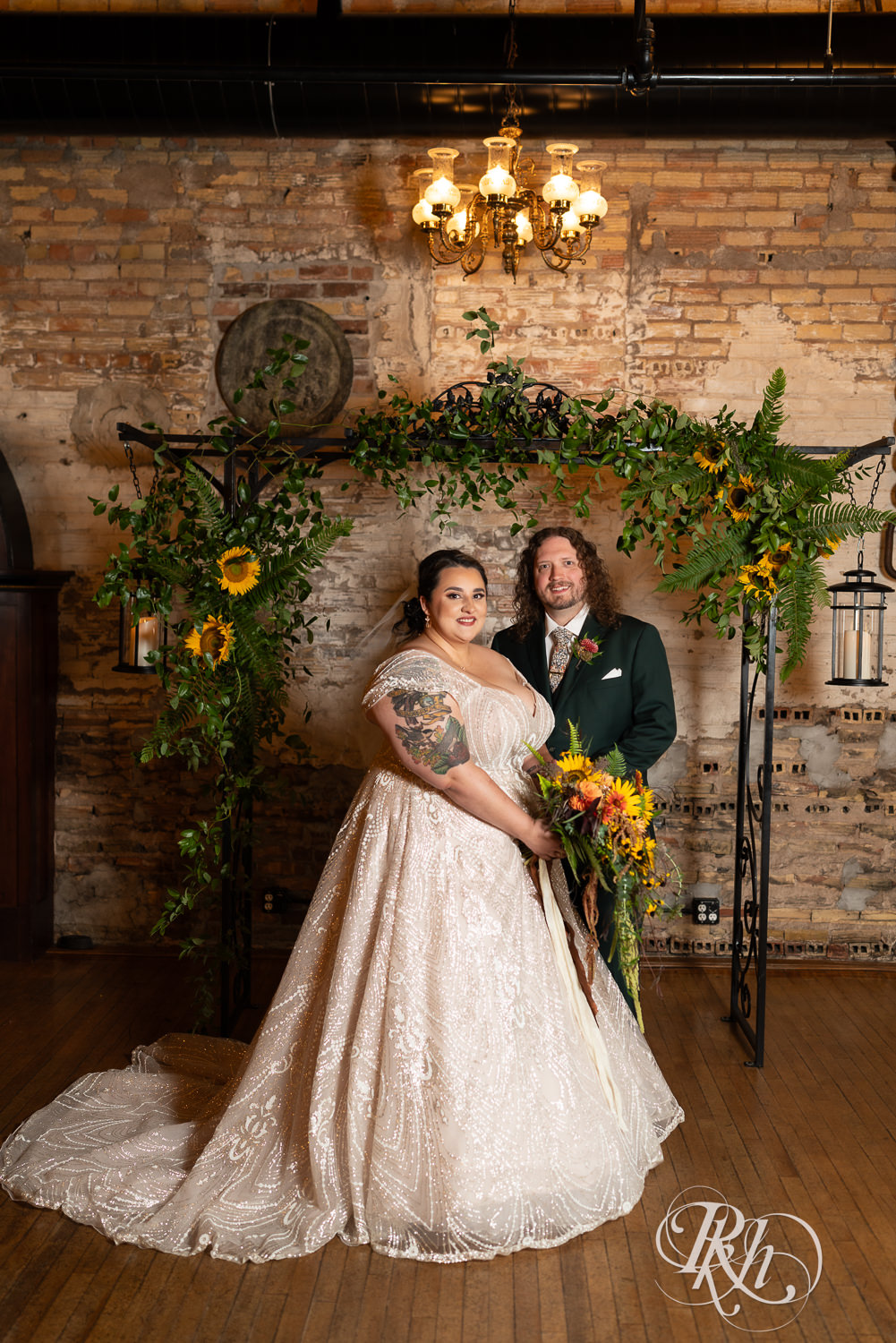 Plus size bride and groom smile in front of flower arch at Kellerman's Event Center in White Bear Lake, Minnesota.