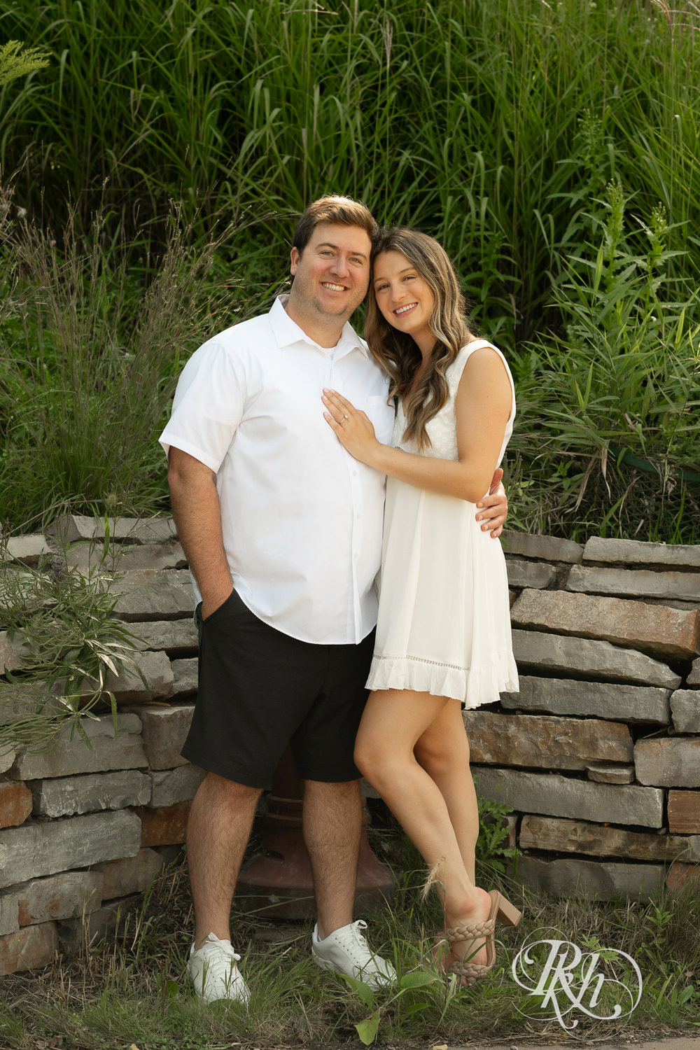 Man and woman in white dress smile during engagement photography at Centennial Lakes Park in Edina, Minnesota.