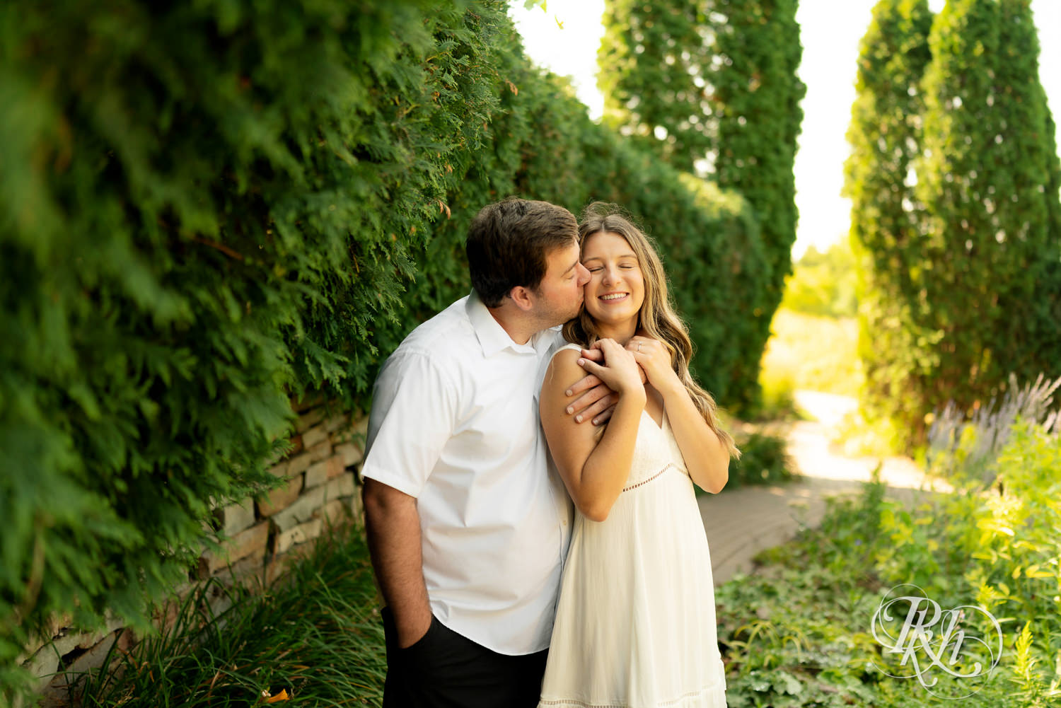 Man and woman in white dress kiss during engagement photography at Centennial Lakes Park in Edina, Minnesota.