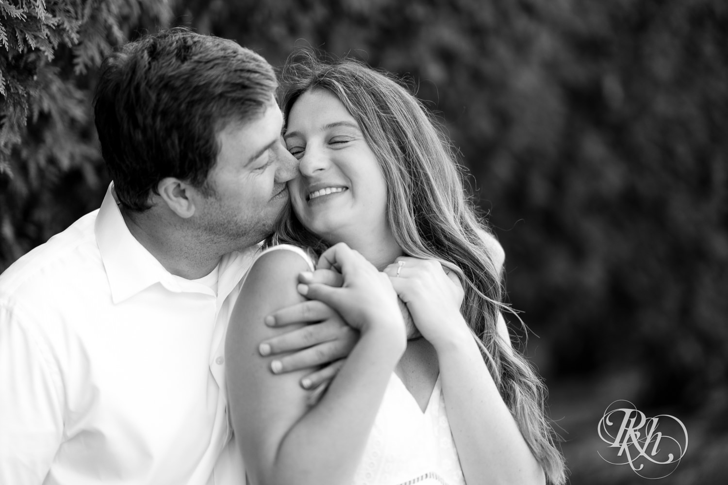 Man and woman in white dress snuggle during engagement photography at Centennial Lakes Park in Edina, Minnesota.