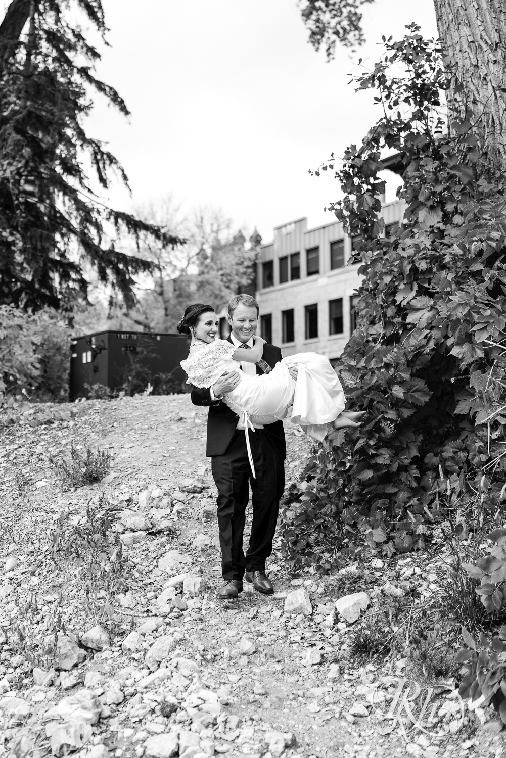 Groom carries bride down a hill on wedding day at The Grand 1858 in Minneapolis, Minnesota.